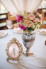 Table number in silver frame with a numeral one, bouquet in metal vase on background
