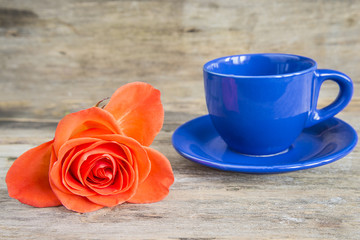 blue coffee cup and scarlet rose on old wooden background with copy space