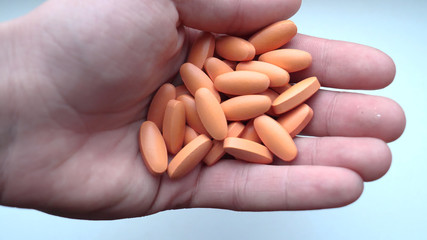 Holds orange capsules, pills or vitamins scattered on a white table.