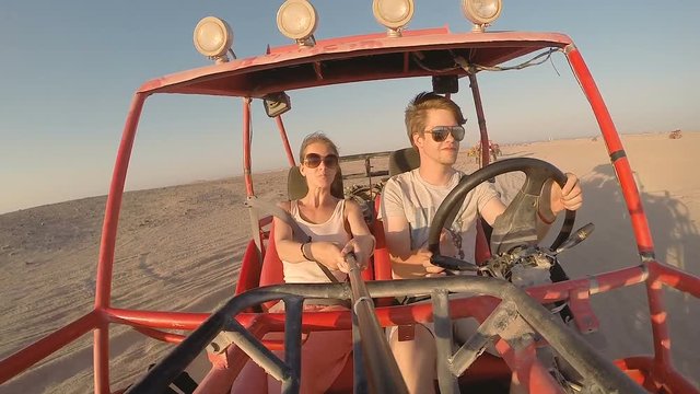 Young traveling couple driving fast through the desert in a dune buggy at sunset
