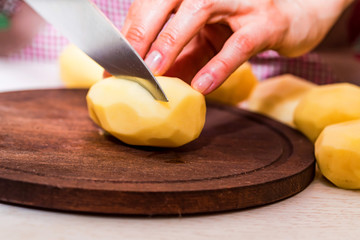 Female hands cut potatoes on wooden board