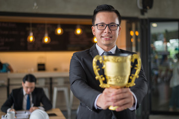 Asian businessman raising up hand and holding a golden trophy cup to cheerful and celebrated his successful in career and mission. concept of winner and competition.