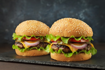 Homemad fast food: two burgers with beef, cheddar, lettuce, onion ang tomato on the slate board.