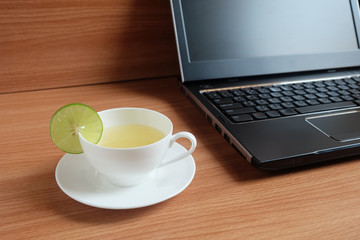 freshly Lime juice in a white cup, and laptop on wooden floor