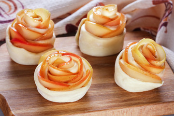 Buns of dough with apple slices, similar to roses on the kitchen board.