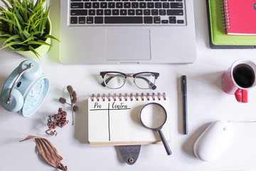 Laptop,spectacle,pen,dried flowers,coffee and a note book written with text PRO and CONTRA on white office table.Creative office table lay out.