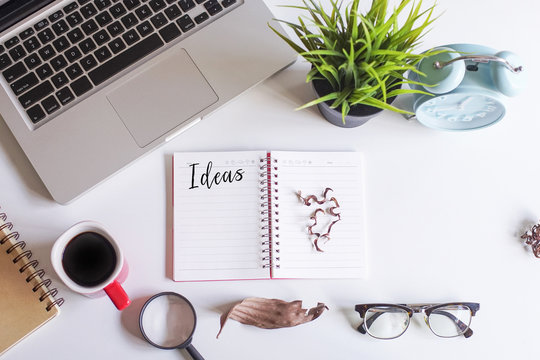 Laptop,coffee,magnifying glass,dried flowers,green plant and notebook written with text IDEAS on white office desk.Creative lay out view from top with copy space.