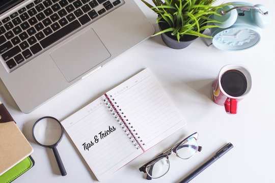 Laptop,coffee,spectacle,pen,magnifying glass and note book written with text TIPS and TRICKS on white office table.Flat Lay photography.