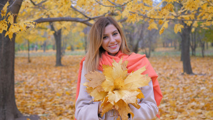 Naklejka na ściany i meble Cute Lady In Beige Coat And Orange Scarf Holding Bouquet Yellow Autumn Leaves