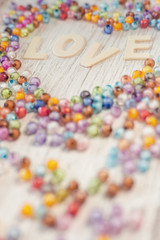 Valentine's day card with "LOVE" text and heap of beads on wooden background,sweet pastel color toned.