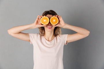 Playful woman in t-shirt posing while holding oranges on eyes
