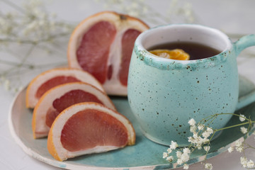 slices of juicy red grapefruit on blue green turquoise bowl mug Cup hot drinks tea coffee healthy Breakfast food meal, and little slices of dried tangerine and white dry flowers background texture