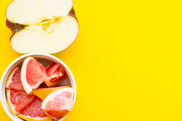 Delicious fruit: fresh juicy apple cut in half and a ceramic bowl with sliced grapefruit on a yellow background with copy space, top view
