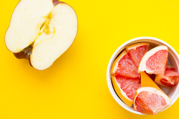 Delicious fruit: fresh juicy apple cut in half and a ceramic bowl with sliced grapefruit on a yellow background with copy space, top view