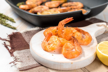 Grilled shrimps with lemon, paprika, spices and herbs on a white wooden board.