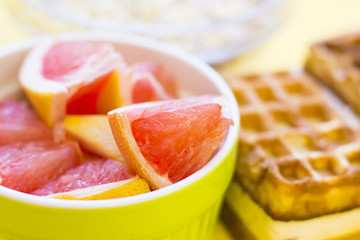 Obraz na płótnie Canvas Delicious breakfast: fresh waffles and a bowl of sliced grapefruit on a yellow background with copy space