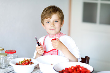 Little blond kid boy helping and making strawberry jam in summer