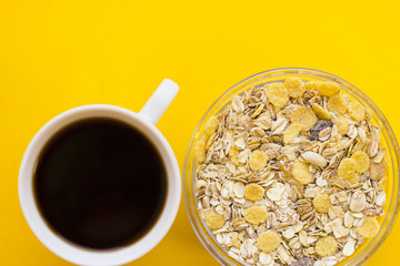 Delicious breakfast: a bowl of cereals and a cup of coffee on a yellow background with copy space