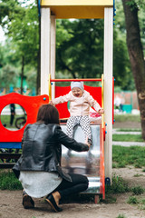 Two year old girl smiling and playing outside with mom at slide