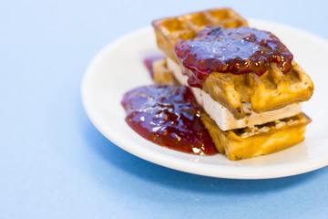 Delicious breakfast: a plate of fresh waffles with raspberry jam on a blue background with copy space