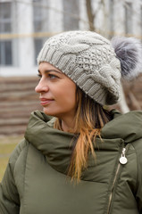 attractive woman in a green winter jacket and hat with a fashionable fur pompom walks