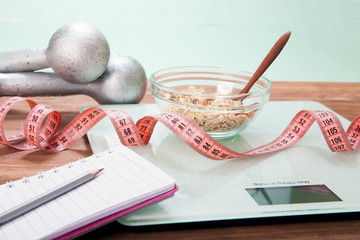 Healthy diet, fitness and weight loss concept. Scales, measuring tape, dumbbells, oatmea on the table.