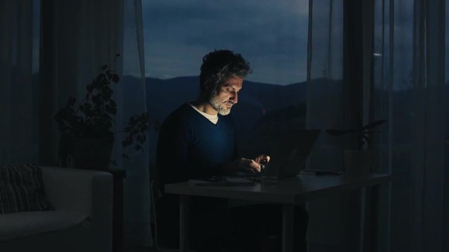 A mature man with laptop working in home office.