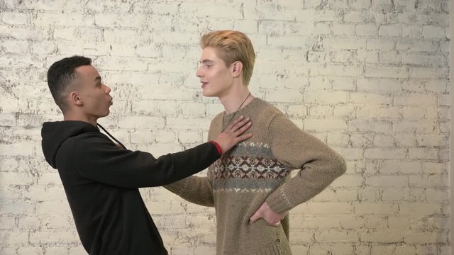 A young American guy with blond hair tries to kiss his African friend, but he is against it. LGBT, homosexuality, gay concept. 60 fps