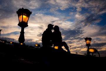 The silhouette of the sensual couple tenderly rubbing noses while sitting on the Chain Bridge near lightning street lamp in Budapest, Hungary.