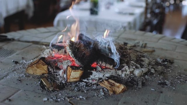 Beautiful and soozing video of calming fire smoldering inside central room fireplace with open chimney design in ski resort restaurant. Winter vacation concept