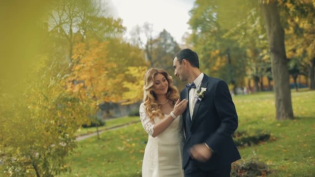 A young and beautiful wedding couple walking together and smiling at each other in the autumn park. Sunny wedding day. Slow motion