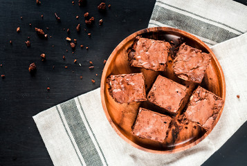 Homemade chocolate brownies on a wooden plate close-up, top view