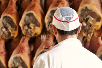 In a ham factory, a man in charge of quality control walks between the hams and controls, the...