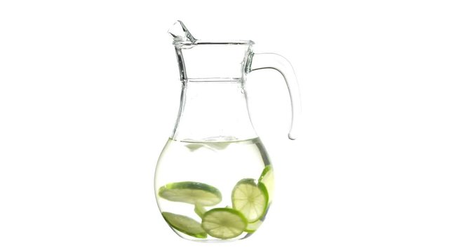 Glass transparent jug with spinning water, ice cubes and lemon limes slices, isolated in the middle of the white background. Clean water, detox and loosing weight concept. Copy space for your text.