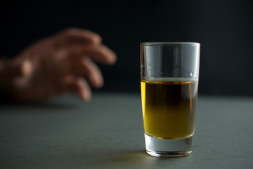 hand reaches for a glass of whiskey or cognac or alcohol drink, alcoholism and alcohol abuse concept, defocused, selective focus, close up, gray table, dark background