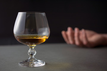 glass of whiskey or cognac or alcohol drink, hand of a drunk man in the background, alcoholism and...