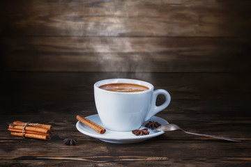 A cup of hot coffee on a dark wooden table and a highlighted background. Low key.