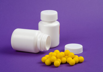 Two plastic bottles of medicines, one of them is without cover and yellow pills with them on a purple background.