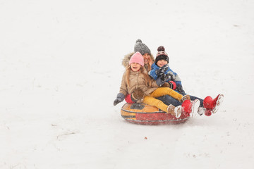 Fototapeta na wymiar Picture of mother with her daughter and son riding tubing in snowfall