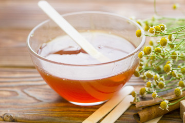 Set of sugaring essentials with natural honey, cinnamon sticks, and camomile on a natural dark wooden background