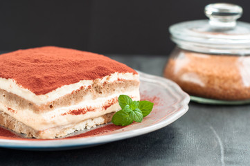 Italian tiramisu dessert on a porcelain plate on a black background