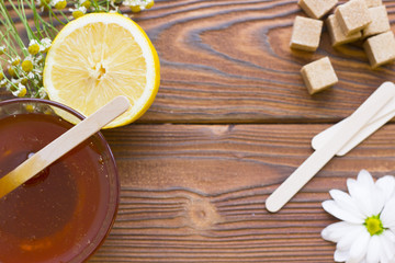 Dark natural wooden background with sugaring essentials: natural honey, medical camomile,lemon, browl sugar cubes and wooden spatulas