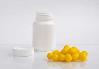 Plastic bottle with medicines without lid and yellow pills next to it on white background.
