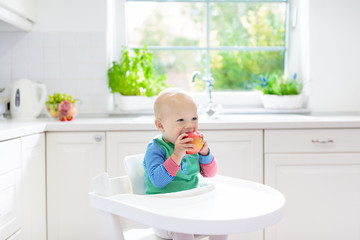 Baby boy eating apple in white kitchen at home