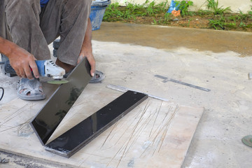 Worker cutting floor tiles with angle grinder at construction site