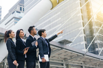 Group of business peoples standing outdoors with office building in the background, point to target