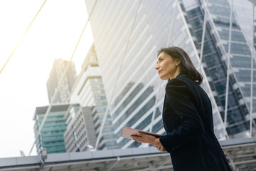 Caucasian businesswoman with wireless tablet standing outdoors with office building in the background, low angle view