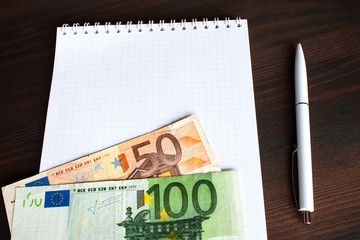 Empty notepad with euro banknote and pen on table