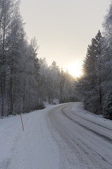 Obraz premium Driving through the winter wonderland in Finland. Sunrise behind the snowy forest.