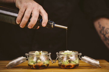 Chef pouring olive oil into the food in a kitchen. Image with black background.
